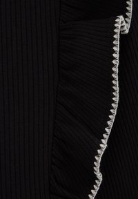 Tessuto nero rigato con bordo arricciato presenta dettagli di cucitura bianchi. La texture è morbida e leggermente elastica, conferendo un aspetto fluido.