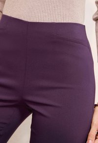Hoge taille paarse broek van rekbaar materiaal, met twee voorzakken en een gladde textuur voor een aansluitende look.
