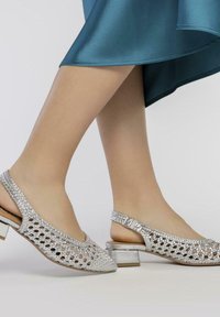 Zapatos slingback plateados con un diseño recortado, adornados con piedras de strass, con un tacón bajo y textura suave.