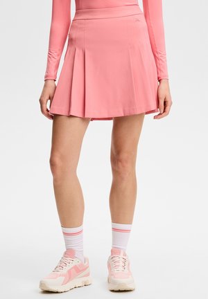Donna che indossa una gonna rosa plissettata, un top a maniche lunghe abbinato, calzini bianchi con strisce rosa e sneaker atletiche rosa e bianche.