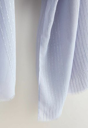 Blødt hvidt stof med lodret tekstureret syning hængende mod en neutral baggrund, der viser detaljeret nærbillede af tekstilfolder og kanter.