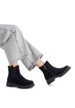 Stivaletti neri in suede con pannelli laterali elasticizzati e chiusura con zip, caratterizzati da una suola in gomma spessa e una finitura testurizzata.