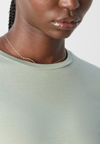 Lys grønn kortermet t-skjorte med rund hals, glatt tekstur og minimalistisk design. Et delikat gullkjede er synlig.