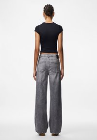 Pelēki platajās kājas džinsi ar augstu jostasvietu, piecu kabatu dizainu un vieglu izbalējušu efektu, kombinēti ar pieguļošu melnu īsām piedurknēm augšu.