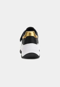 Baskets noires et dorées avec une épaisse semelle blanche, vue arrière, montrant la semelle extérieure noire texturée et le logo "GUESS" en relief sur le talon.