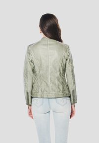 Chaqueta de cuero verde con diseño entallado, detalles texturizados y hombros acanalados. Puños con cremallera y acabado liso completan el look.