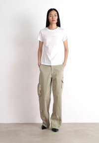 Witte T-shirt met korte mouwen en ronde hals, gecombineerd met beige cargobroek, voorzien van zijzakken en een glanzend accent op de bovenbeen.