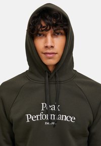 Dunkelgrüner Hoodie mit Kängurutasche, Kapuze mit Kordelzug und weißem besticktem Text "Peak Performance" und "Est. 1986."