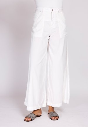 High-waisted wide-leg white pants with front patch pockets worn with black and white woven open-toe flat sandals.