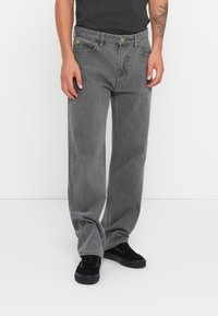 Grå denim jeans med en afslappet pasform, der har grønne detaljer og forlommer. Materialet har en blød tekstur med en let afdæmpet finish.
