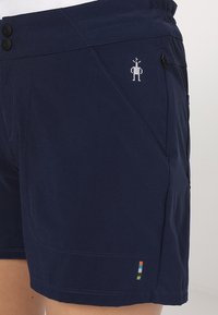 Námořnické šortky z lehké tkaniny s dvěma černými knoflíky, boční kapsou a grafickým potiskem na přední straně. Mají barevný blok jako zdobení.