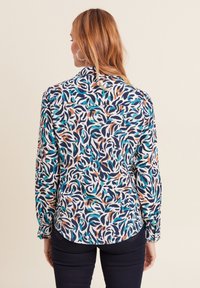 Blusa a maniche lunghe in tessuto stampato con colori vorticosi di blu, arancione e bianco. Texture liscia con polsini abbottonati e orlo curvato.