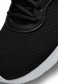 Gros plan sur une basket en tissu tricoté noir avec des lacets noirs et une semelle blanche.