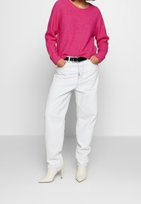 Suéter de punto magenta, jeans de mezclilla clara de tiro alto, cinturón negro con herrajes plateados, botas de tobillo en crema con punta afilada.