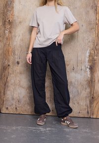 T-shirt beige en coton à manches courtes associée à un pantalon noir ample. La tenue est complétée par des chaussures de sport marron.