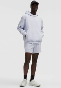 Lys blå hættejakke med frontlomme, parret med matchende shorts. Har ribbede manchetter og en logo detalje. Hvide atletiske sko og en sort kasket.