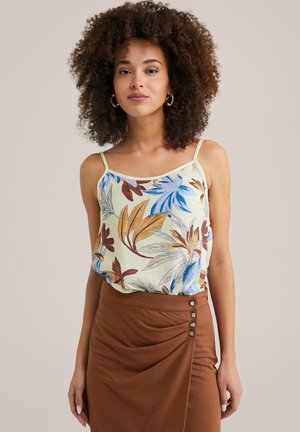 Camisole floral de couleur jaune clair avec des feuilles bleues et brunes, dotée de fines bretelles. Accompagnée d'une jupe brune à accents de boutons.
