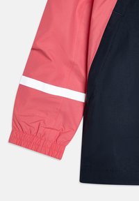 Μανίκι μπουφάν σε κόκκινο και ναυτικό μπλε με ελαστικό τελείωμα, που διαθέτει μια λευκή ανακλαστική λωρίδα πάνω στο κοραλλί τμήμα και έχει λείο, ελαφρύ υφή.