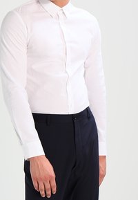 Bílá košile s dlouhými rukávy, klasickým límcem a hladkým povrchem. V kombinaci s tmavomodrými kalhotami, které představují elegantní střih.