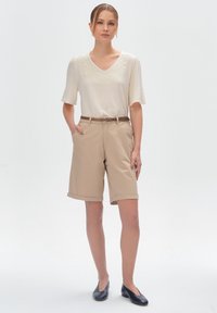 Beżowe szorty z podwiniętymi nogawkami, w połączeniu z jasnym, krótkim topem z delikatnym haftem. Całość dopełniają czarne mokasyny.
