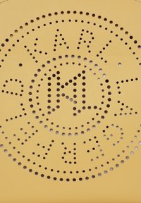 Gul perforeret læder med udskaaret logo-design. Har et cirkulært mønster af huller omkring initialerne "KL." Glat tekstur.