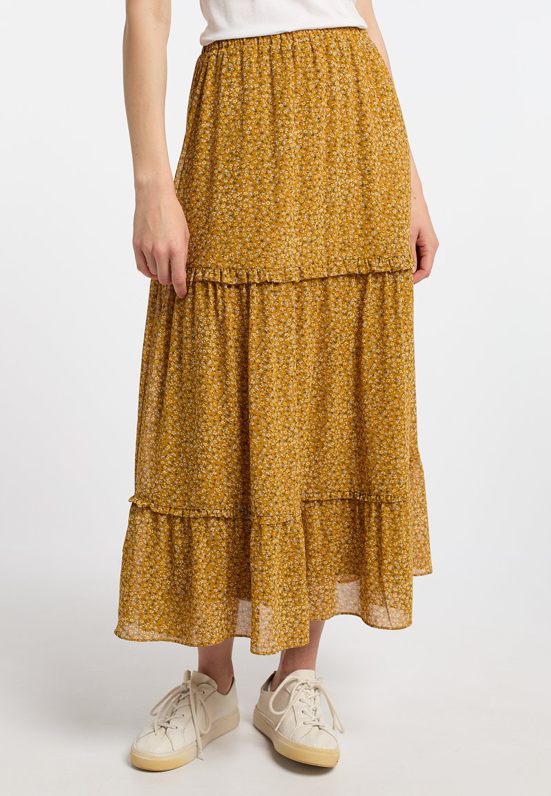 Gonna maxi a balze gialla con motivo floreale, orlo arricciato, fascia elastica in vita e tessuto leggero. Indossata con sneakers bianche.