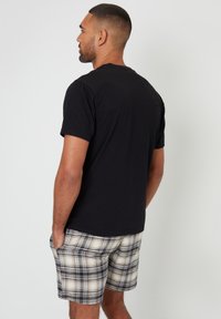 Sort crew-neck t-shirt med korte ærmer parret med rudemønstret shorts i beige, sort og hvid. Shortsene har lommer og en tekstureret stof.