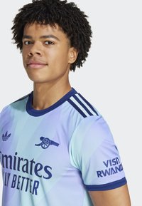 Lys blå sports trøje med mørkeblå accenter, der har diagonalt grafisk design, logo og branding "VISIT RWANDA" på ærmet.