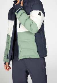 Puffer jacket featuring a color-block design in navy, white, and light green. Made of shiny material with a zip closure and adjustable cuffs.