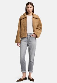 Giacca beige e morbida con colletto, zip frontale e maniche larghe. Abbinata a jeans grigio chiaro e ballerine nere con stampa leopardata.
