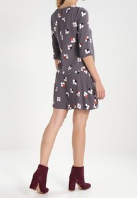 Robe florale grise à manches trois-quarts, présentant des motifs floraux colorés. Associée à des bottines bordeaux avec des accents de boutons.