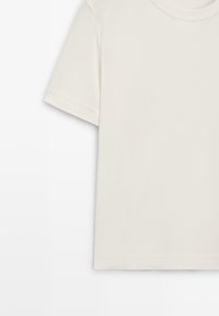 T-shirt en coton écru à manches courtes avec col rond, vu de face avec la manche gauche et l'épaule visibles.