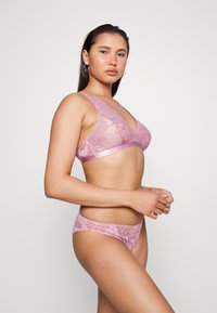 Conjunto de lingerie de renda em rosa claro, apresentando um sutiã com decote em V profundo e alças ajustáveis, combinado com uma parte de baixo de renda correspondente.