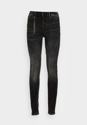 Schwarze Skinny-Jeans mit hoher Taille, Knopfverschluss und einem silbernen Kettendetail, das nahe der rechten vorderen Tasche hängt.