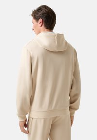Beige mikina s kapucí, volného střihu, měkké textury, žebrované manžety a lem. Viditelné švy jako akcenty a jednoduchý design.
