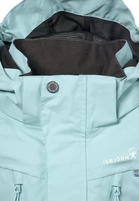 Lys blå jakke med en lynlåslomme, mesh-foring og logo-detail. Har en knaplukning og glat, vandafvisende stof.