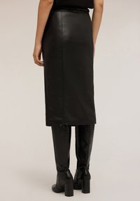 Fustă midi din piele neagră cu o textură netedă și o siluetă dreaptă. Dispune de o deschidere pe spate și este combinată cu cizme până la genunchi, cu embossing crocodil.
