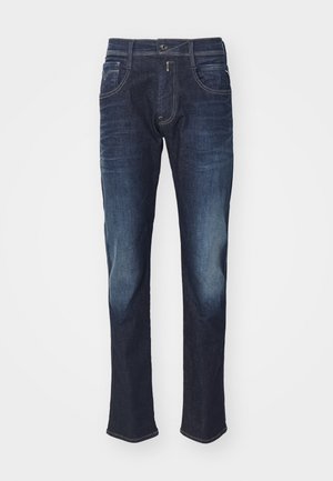 Dark blue denim jeans with front pockets, button, and subtle faded areas on thighs and knees against a plain light background.