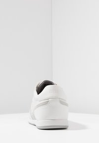 Bílé kožené tenisky s šedými semišovými akcenty a textilní podšívkou. Vyznačují se nízkým profilem a minimalistickým designem. Logo na patě.