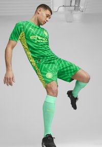 Zöld foci szerelés, texturált mintával, logóval a mellkason és sárga kiegészítőkkel. Tartalmazza a hozzáillő menta zöld zoknikat és fekete stoplis cipőt.