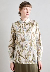 Camicia a maniche lunghe con un motivo che presenta una combinazione di foglie verdi e dettagli blu su uno sfondo beige chiaro. Colletto con bottoni e texture morbida.