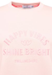 Helles rosa Sweatshirt mit strukturiertem Stickerei, die den Text "HAPPY VIBES" über "SHINE BRIGHT" zeigt. Etikett im Halsbereich sichtbar.