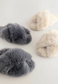 Faux fur slippers in gray and cream, featuring a cross-band design. Soft, plush texture with rounded shape and flat soles.