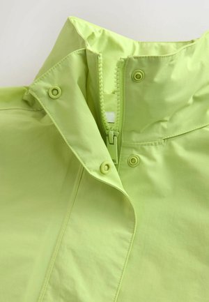Light green jacket collar with visible zipper partially unzipped and three snap buttons on the flap.