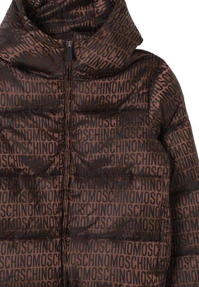 Bruine pufferjas met capuchon, bedekt met herhaalde zwarte "MOSCHINO" tekstpatroon, met een rits aan de voorkant.