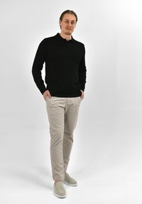 Zwarte longsleeve polo, beige slim-fit broeken en lichtgrijze instapschoenen, staand op een neutrale achtergrond.