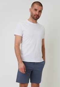 Weißes Kurzarm-T-Shirt kombiniert mit dunkelblauen Shorts. Das T-Shirt hat einen runden Ausschnitt, und die Shorts verfügen über Taschen und einen geraden Schnitt.
