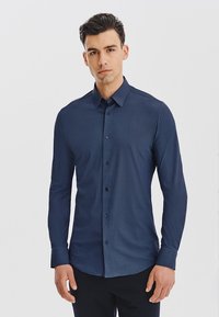 Granatowa koszula z długim rękawem o teksturowanym wzorze, z zapięciem na guziki i kołnierzykiem. Wykonana z lekkiego materiału. Potrafi zapewnić dopasowany krój.