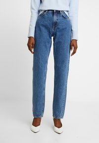 Blå denimjeans med hög midja, rak benpassform och klassisk femficksdesign. Sparas med en ljusblå tröja och vita klackar.