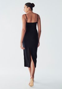 Black midi dress with thin straps, body-hugging design, side slit, and ruching details. Smooth fabric with a matte finish.